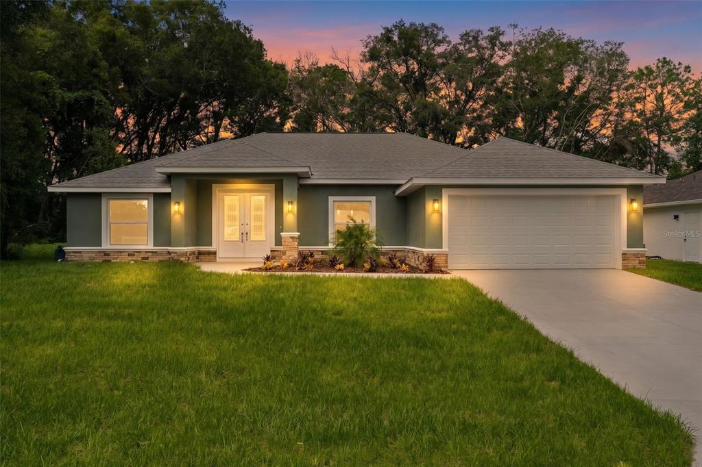 A single-story house with green siding, stone accents, and a two-car garage at dusk — 8277 SE 158TH STREET, SUMMERFIELD, FL