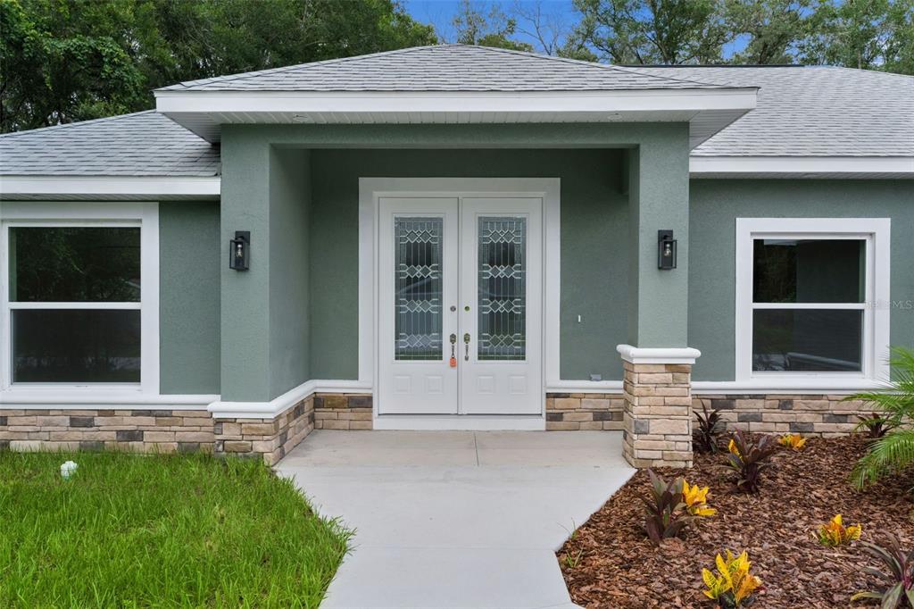 The exterior of a house features a green stucco facade, stone veneer, and double front doors — 8277 SE 158TH STREET, SUMMERFIELD, FL