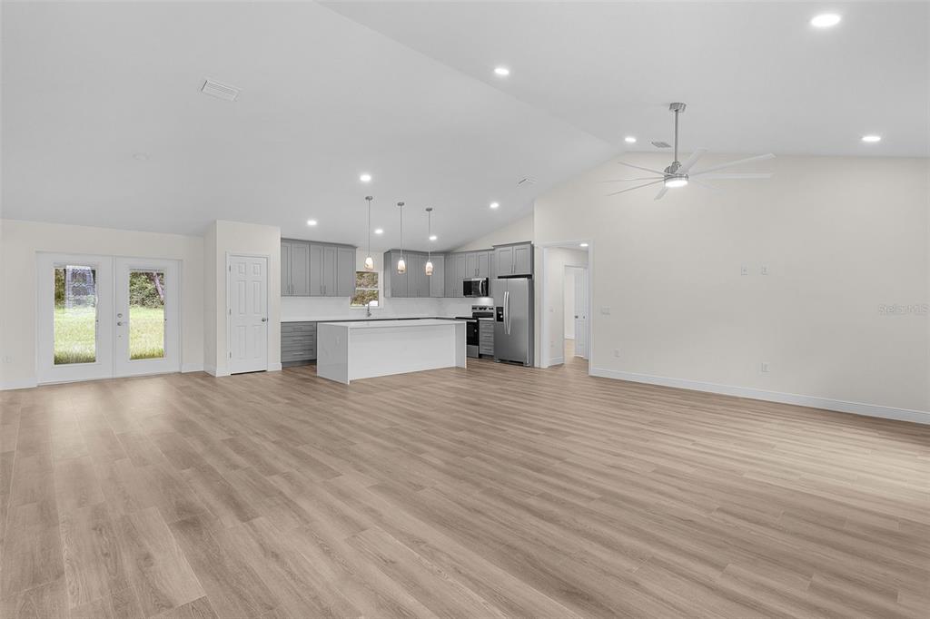An open-concept kitchen and living area features light wood flooring, gray cabinetry, and a white island — 8277 SE 158TH STREET, SUMMERFIELD, FL