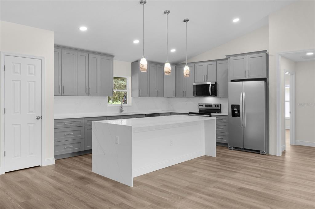 A modern kitchen features gray cabinets, white quartz countertops, a central island, and stainless appliances — 8277 SE 158TH STREET, SUMMERFIELD, FL