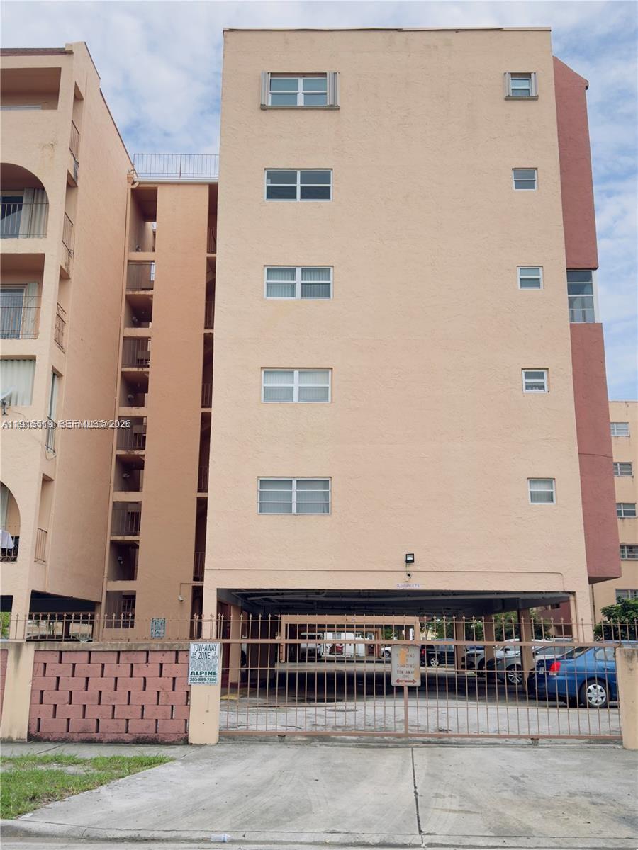 A multi-story tan apartment building features a ground-level parking area enclosed by a metal gate — 440 E 23rd St # 1305, Hialeah FL 33013, HIALEAH, FL