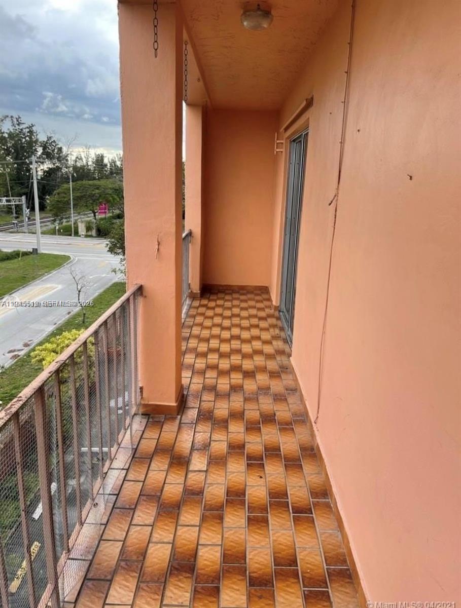 A narrow balcony with brown tiled flooring overlooks a street and green space — 440 E 23rd St # 1305, Hialeah FL 33013, HIALEAH, FL