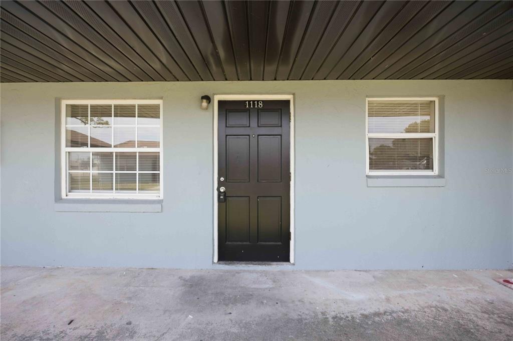 A black front door with the number 1118 is centered between two windows on a building — 1118 MELODY LANE, SEBRING, FL
