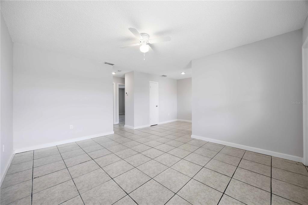 An empty room features light gray walls, a white ceiling fan, and beige tiled flooring — 1118 MELODY LANE, SEBRING, FL
