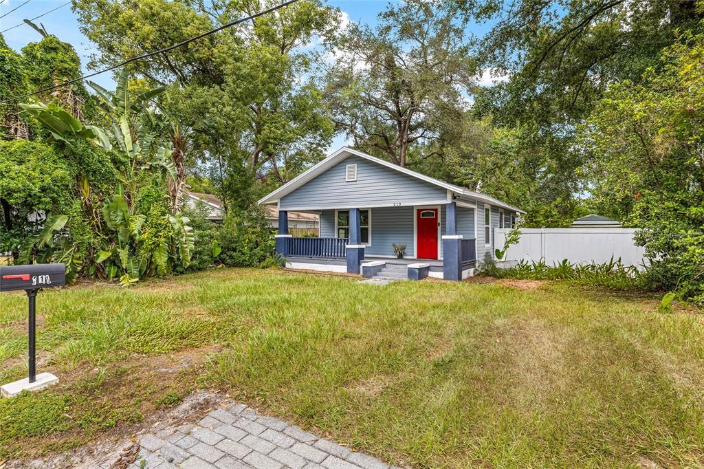 A blue bungalow with a red front door and a covered porch sits on a lawn — 210 E CLUSTER AVENUE, TAMPA, FL