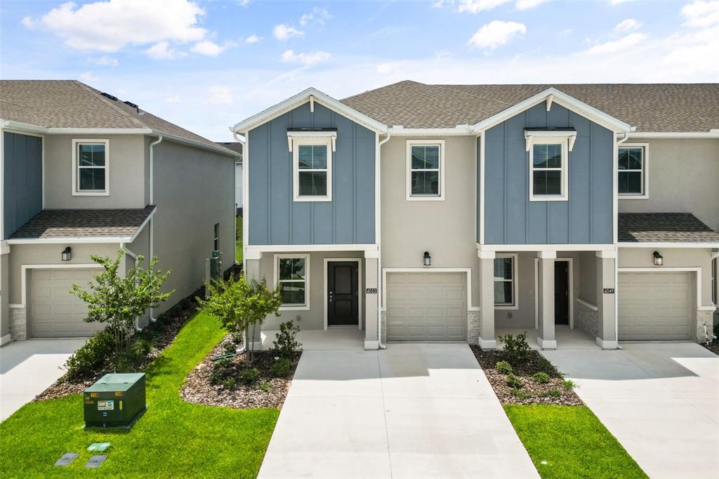 A row of modern two-story townhouses features gray stucco, blue siding, and attached garages — 6053 ZEN WAY, CLERMONT, FL