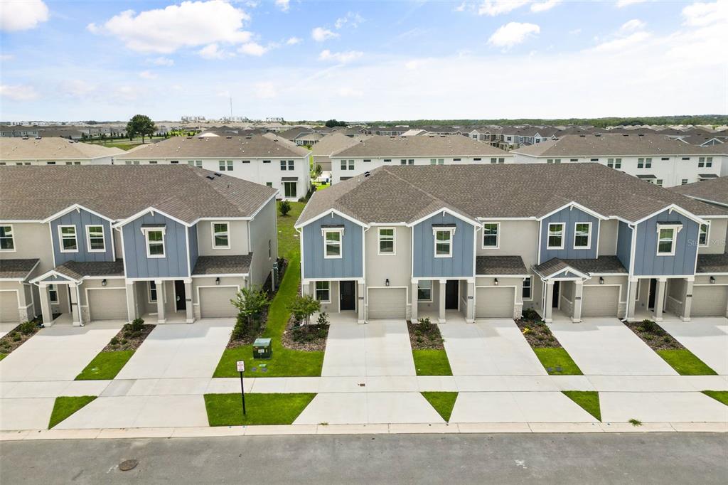 An aerial view of a row of modern two-story townhouses with attached garages and driveways — 6053 ZEN WAY, CLERMONT, FL
