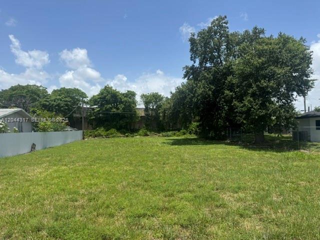 A grassy, vacant residential lot is bordered by a white fence and mature trees — 10420 NW 6 AVE, Miami FL 33150, MIAMI, FL