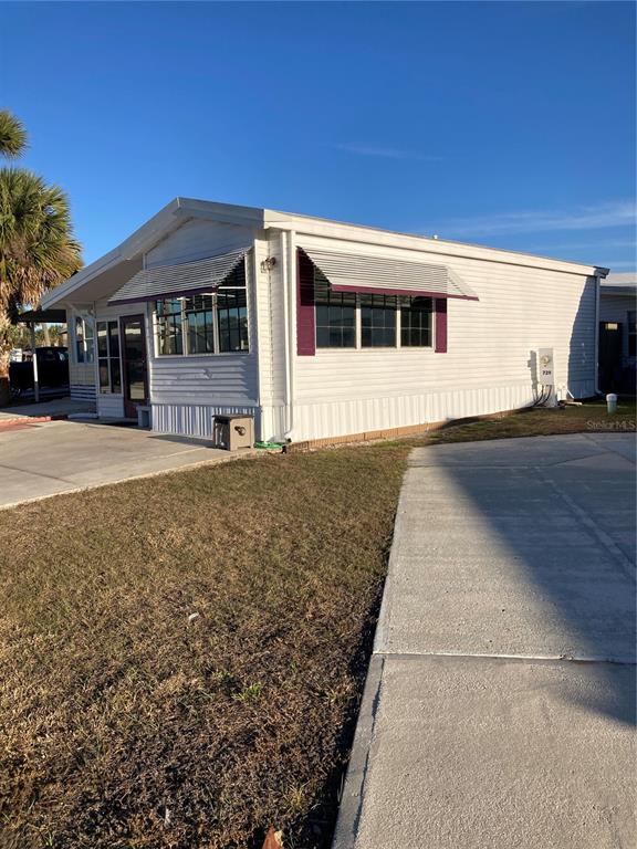 The exterior of a white mobile home features metal awnings over the windows and a driveway — 9000 US HIGHWAY 192 UNIT 729, CLERMONT, FL