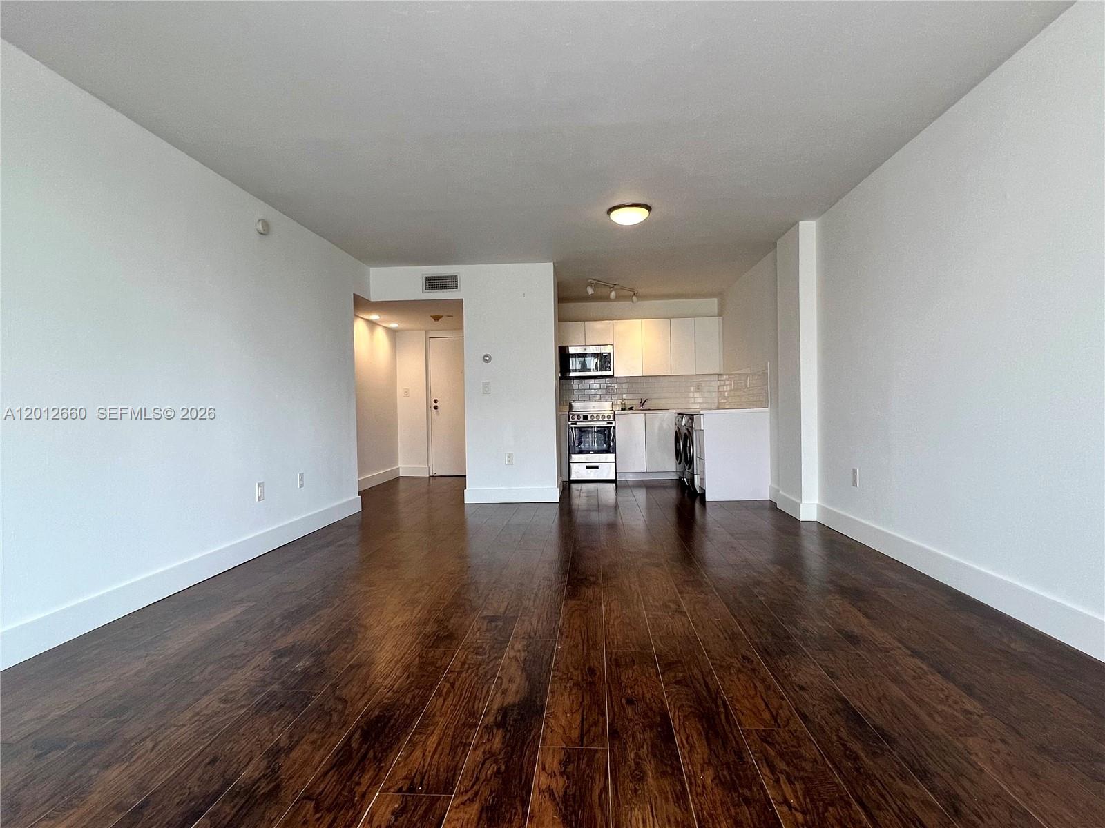 An open-concept living area features dark wood flooring, white walls, and a compact kitchen — 5055 NW 7th St # 303, Miami FL 33126, MIAMI, FL