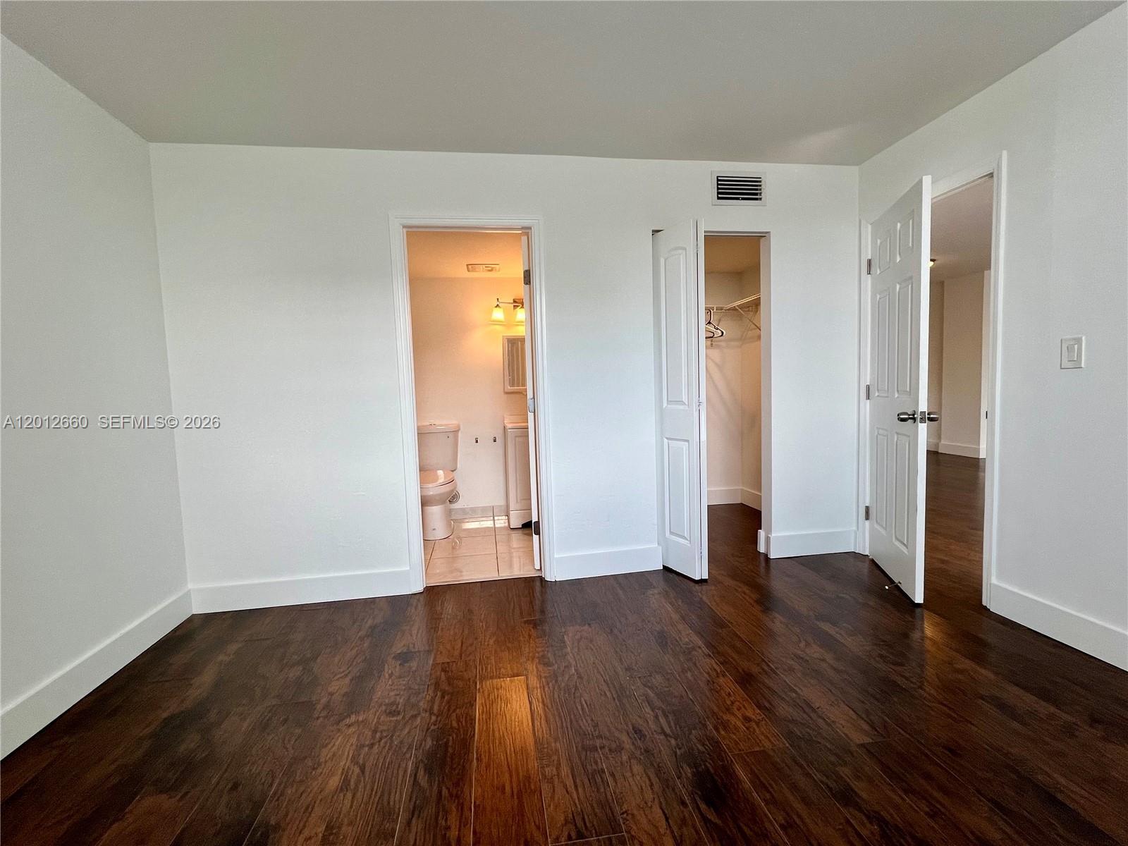 A bedroom features dark wood flooring, a bathroom entrance, a closet, and an open doorway — 5055 NW 7th St # 303, Miami FL 33126, MIAMI, FL