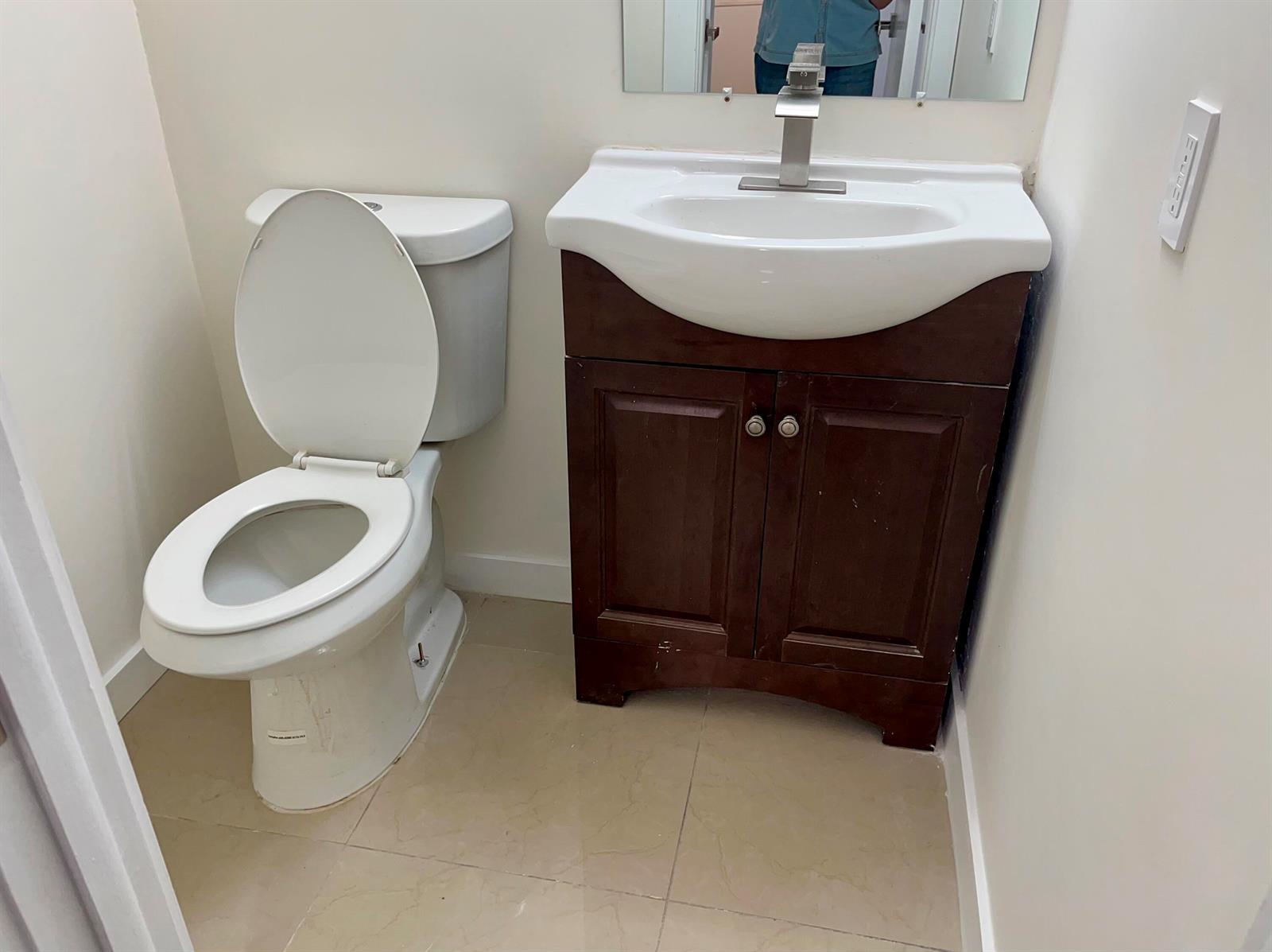 A small bathroom features a white toilet, a dark wood vanity, and a wall mirror — 1801 S Ocean Drive # 633, Hallandale Beach FL 33009, HALLANDALE BEACH, FL