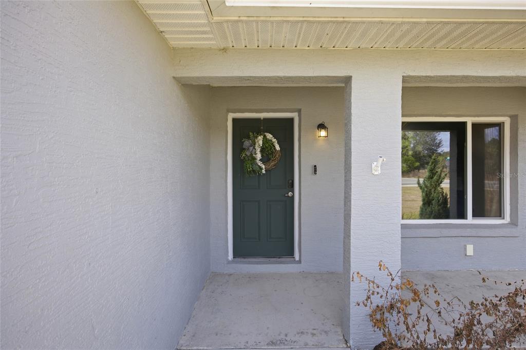 A gray exterior wall features a dark green front door with a wreath and porch — 224 FISHER ROAD, OCKLAWAHA, FL