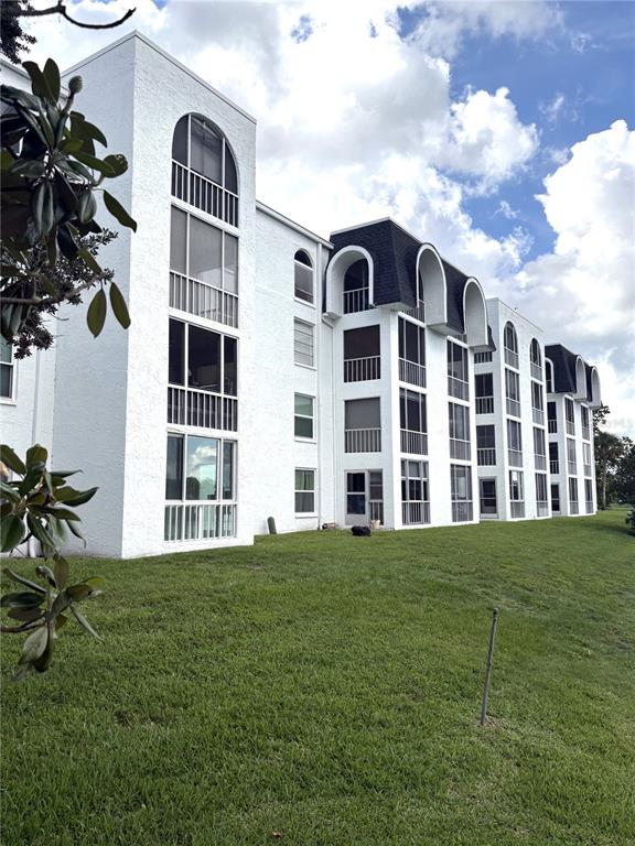 A multi-story white apartment building with arched balconies stands above a grassy lawn — 1200 37TH STREET N UNIT 107, ST PETERSBURG, FL