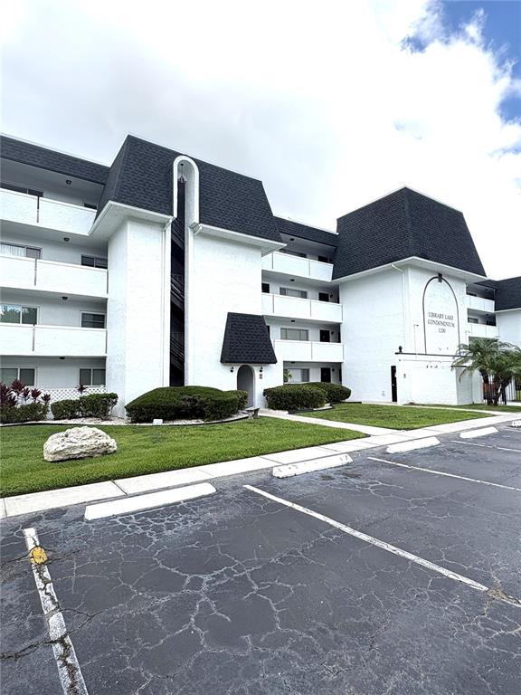 A multi-story white condominium building features dark shingled roofs and a paved parking lot — 1200 37TH STREET N UNIT 107, ST PETERSBURG, FL