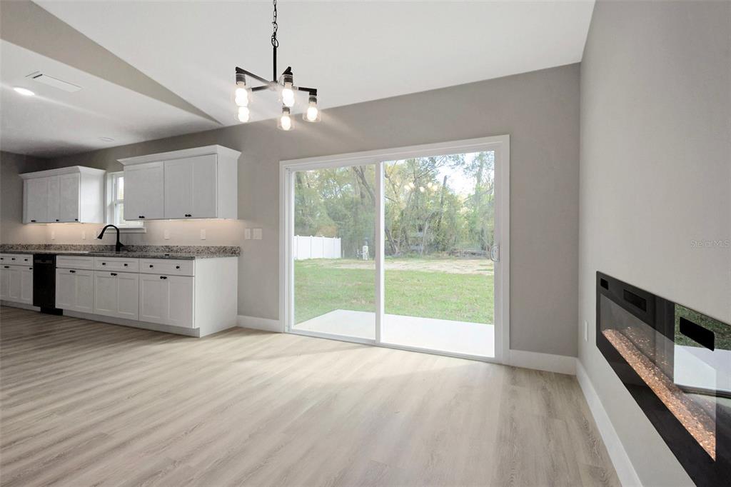 A galley kitchen features white cabinets, granite countertops, stainless steel appliances, and light wood flooring — 6938 SE 122ND LANE, BELLEVIEW, FL