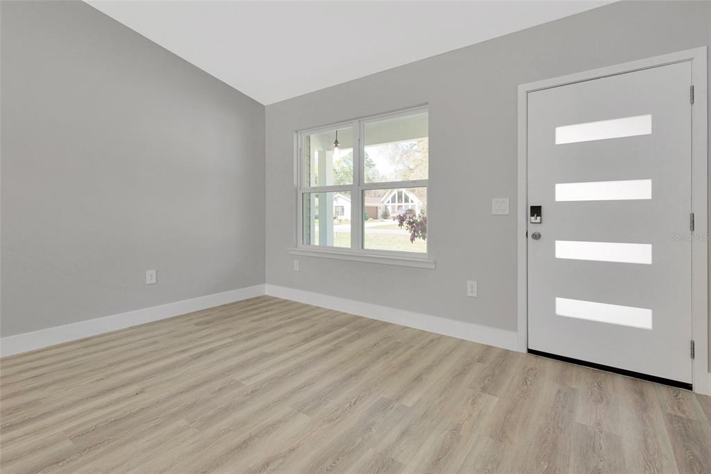 A living room with light gray walls, wood-look flooring, a ceiling fan, and a front door — 6938 SE 122ND LANE, BELLEVIEW, FL