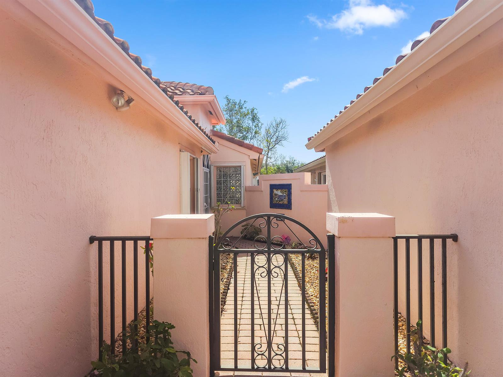 A paved walkway leads through a metal gate between two pink stucco exterior walls — 5122 Corbel Lake Way, Boynton Beach FL 33437, BOYNTON BEACH, FL
