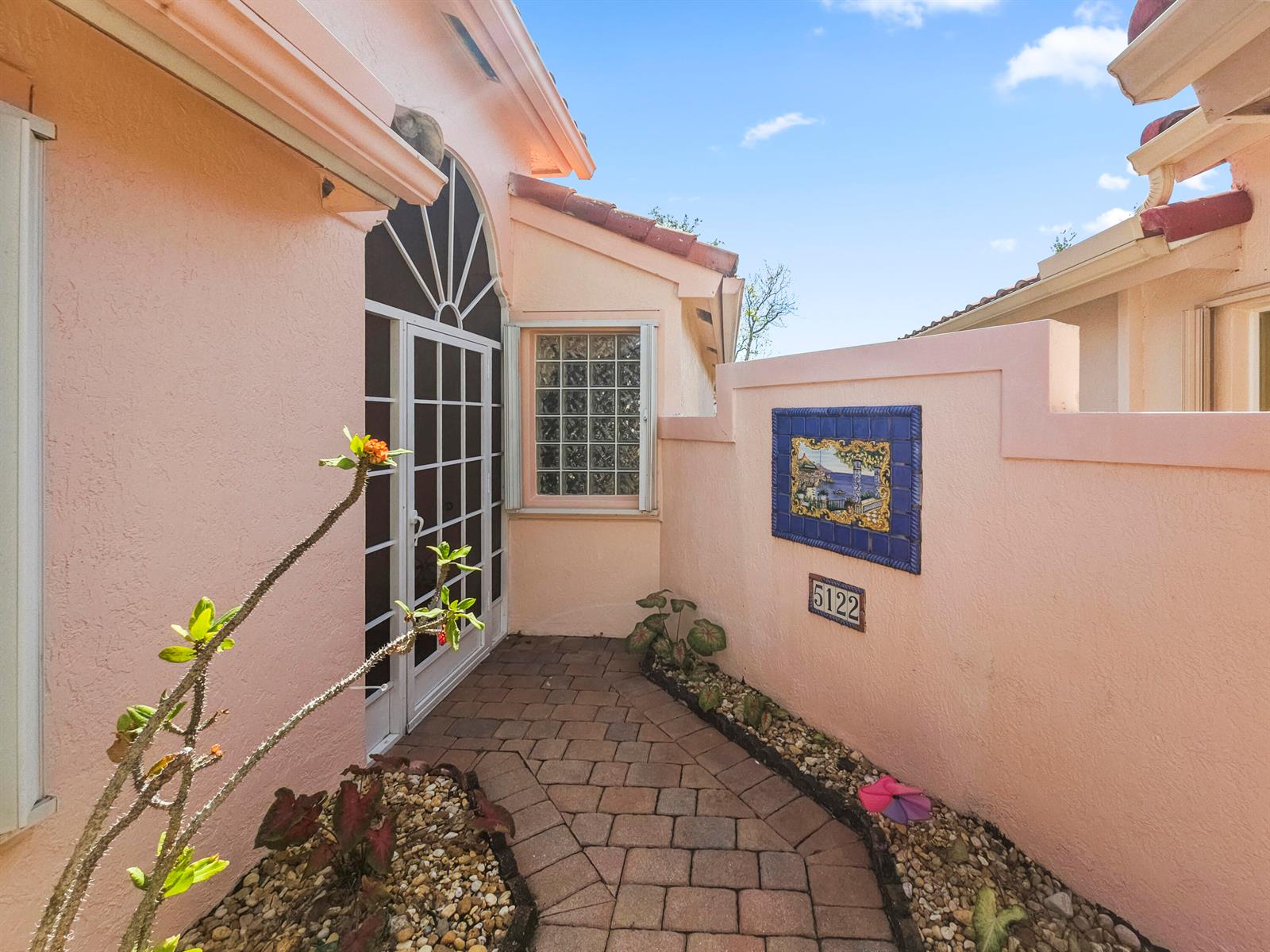 A pink stucco exterior features a brick walkway leading to a glass-paned door and window — 5122 Corbel Lake Way, Boynton Beach FL 33437, BOYNTON BEACH, FL