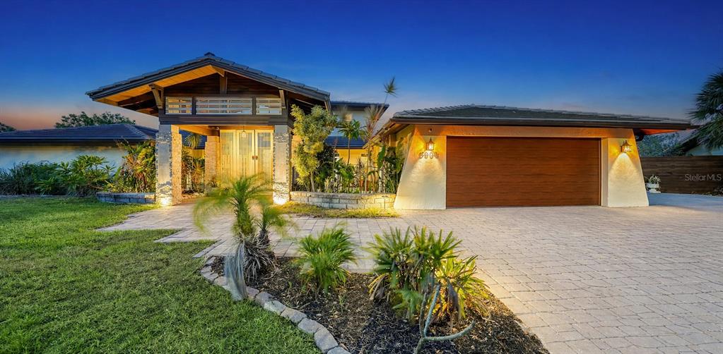 A modern single-story house with a large garage, stone accents, and a paved driveway at dusk — 5500 MERRIMAC DRIVE, SARASOTA, FL