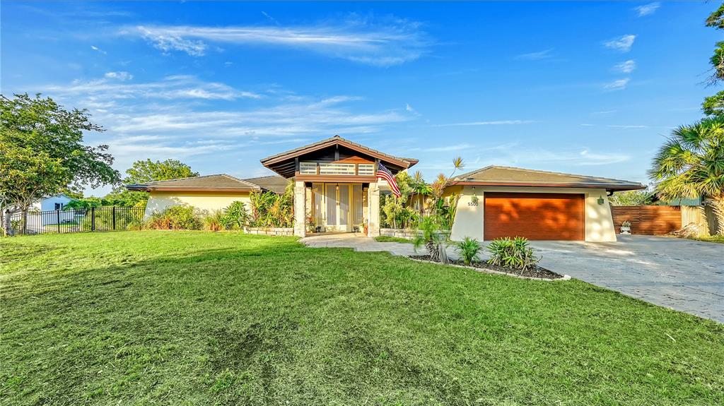 A single-story house with a wooden garage door and a front porch under a roof — 5500 MERRIMAC DRIVE, SARASOTA, FL