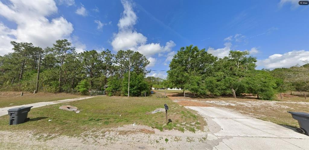 A vacant, grassy lot with a concrete driveway, scattered trees, and a mailbox — COMMONWEALTH AVE N, POLK CITY, FL
