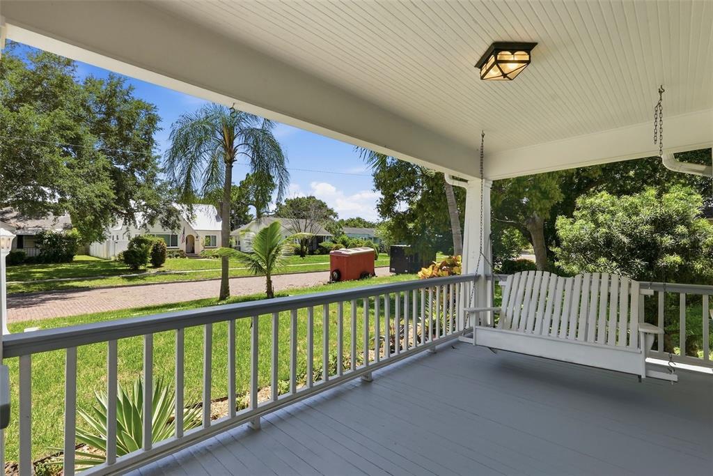 A covered front porch features a white wooden swing, gray flooring, and a railing — 4227 2ND AVENUE N, ST PETERSBURG, FL
