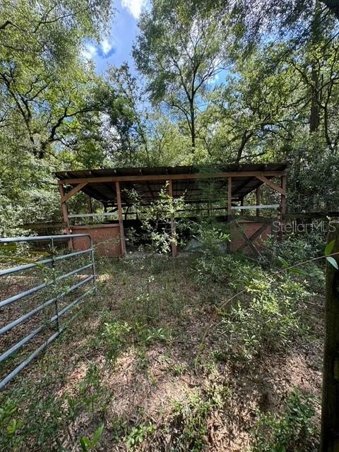 An open-sided wooden barn structure stands in a wooded area behind a metal gate — SW COLES COURT, FORT WHITE, FL