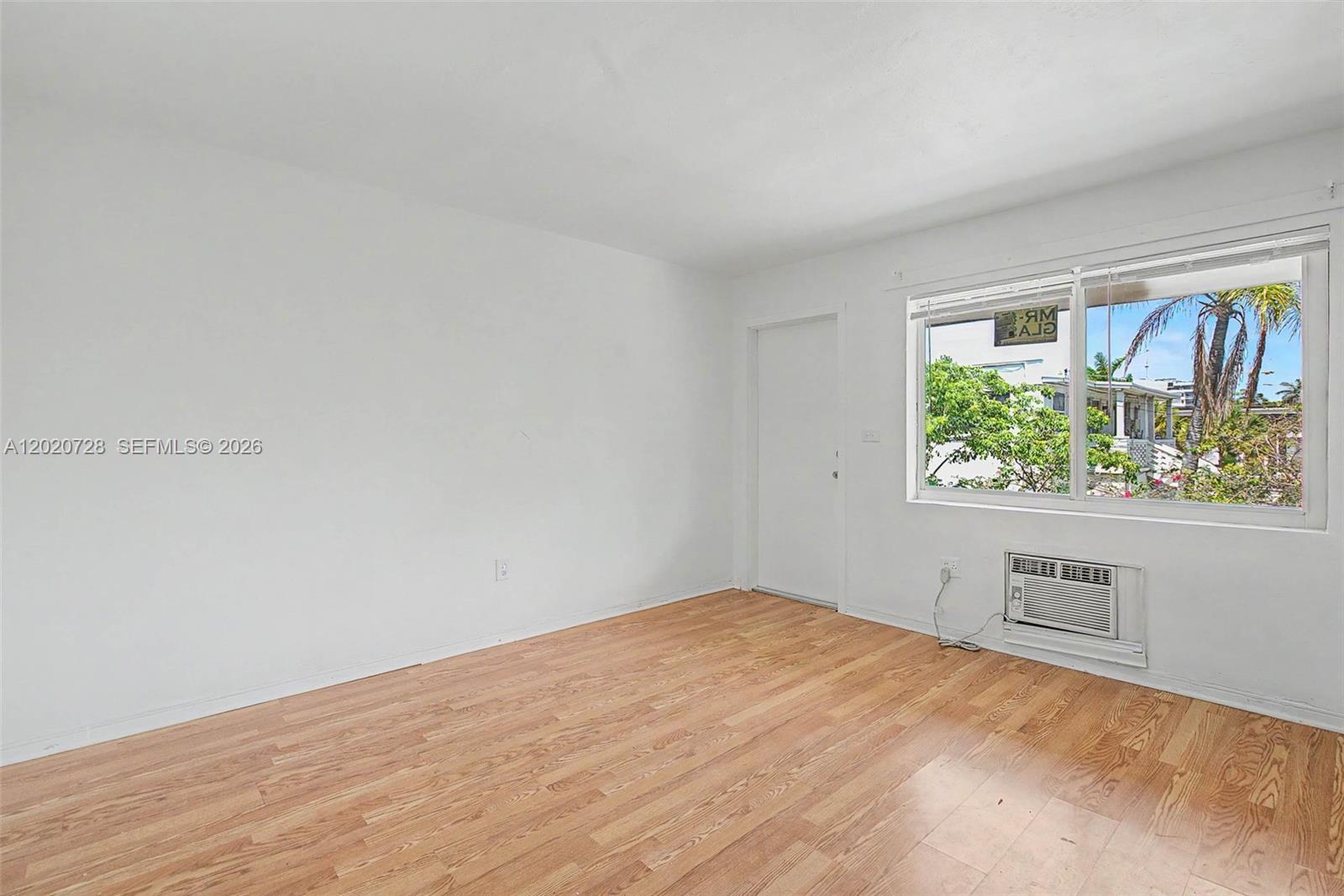 An empty room features white walls, light wood flooring, a window, and a wall-mounted air conditioner — 60 NW 79th St # 6, Miami FL 33150, MIAMI, FL