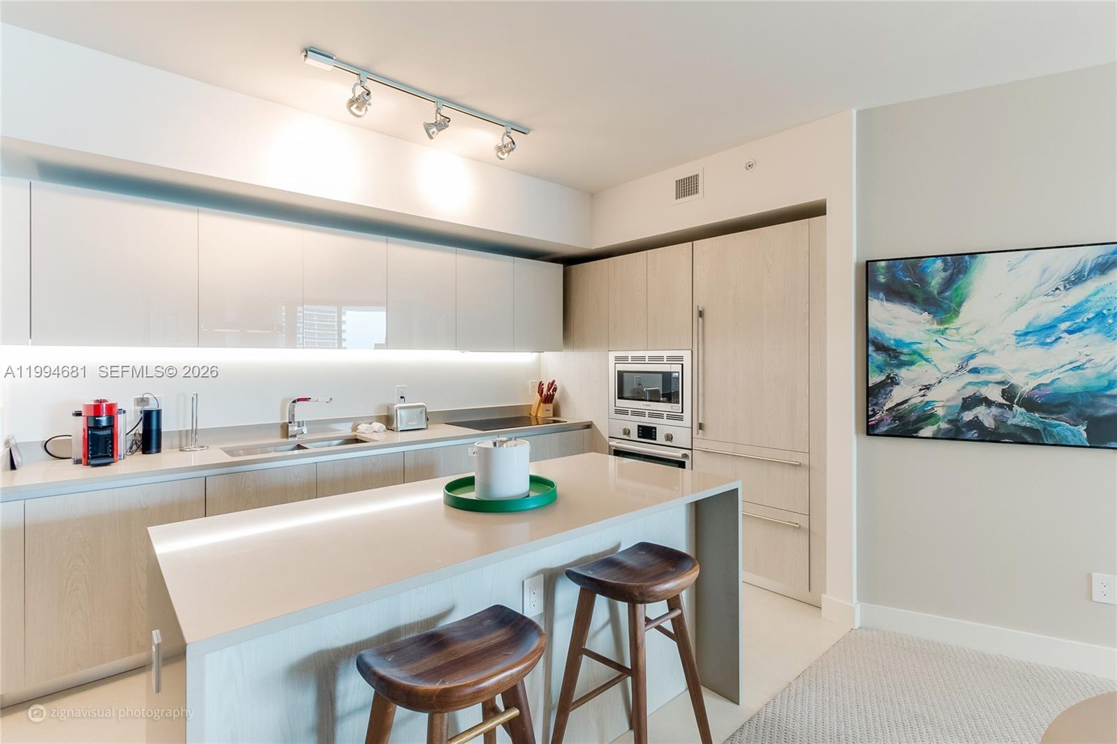 A modern kitchen features light wood cabinetry, a central island with bar stools, and track lighting — 4111 S Ocean Dr # 2707, Hollywood FL 33019, HOLLYWOOD, FL