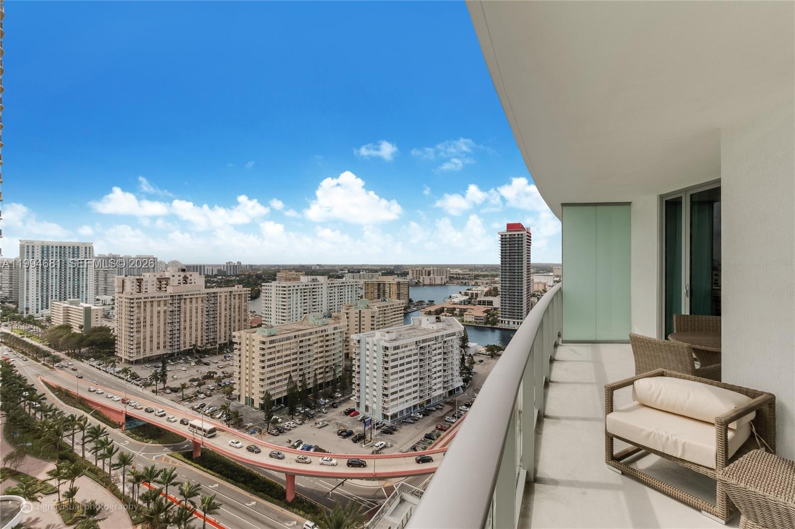 A high-rise balcony with wicker furniture overlooks a city skyline, a highway, and a waterway — 4111 S Ocean Dr # 2707, Hollywood FL 33019, HOLLYWOOD, FL