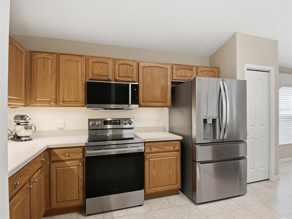 A kitchen features oak cabinets, stainless steel appliances, and white countertops — 1332 CAMERO DRIVE, THE VILLAGES, FL