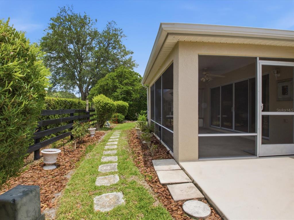 A screened-in patio sits beside a stone walkway and a black wooden fence — 1332 CAMERO DRIVE, THE VILLAGES, FL
