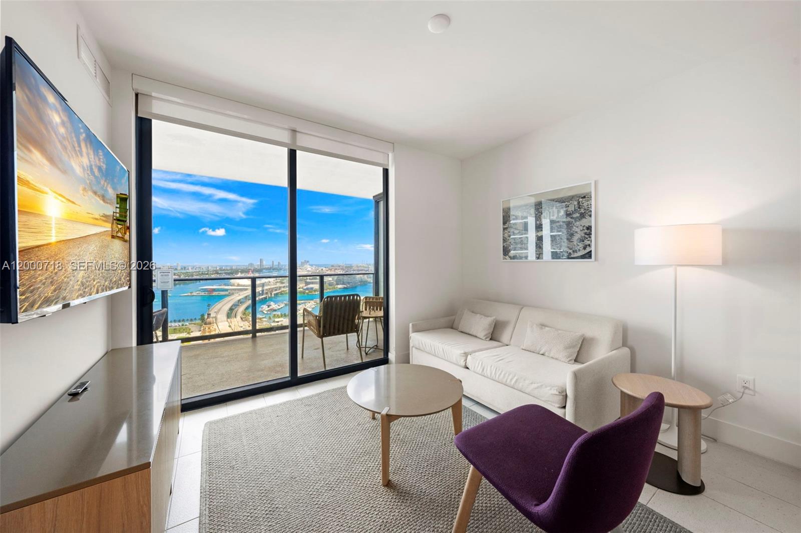 A modern living room features a sofa, purple chair, television, and a balcony with water views — 159 NE 6th St # 2915, Miami FL 33132, MIAMI, FL