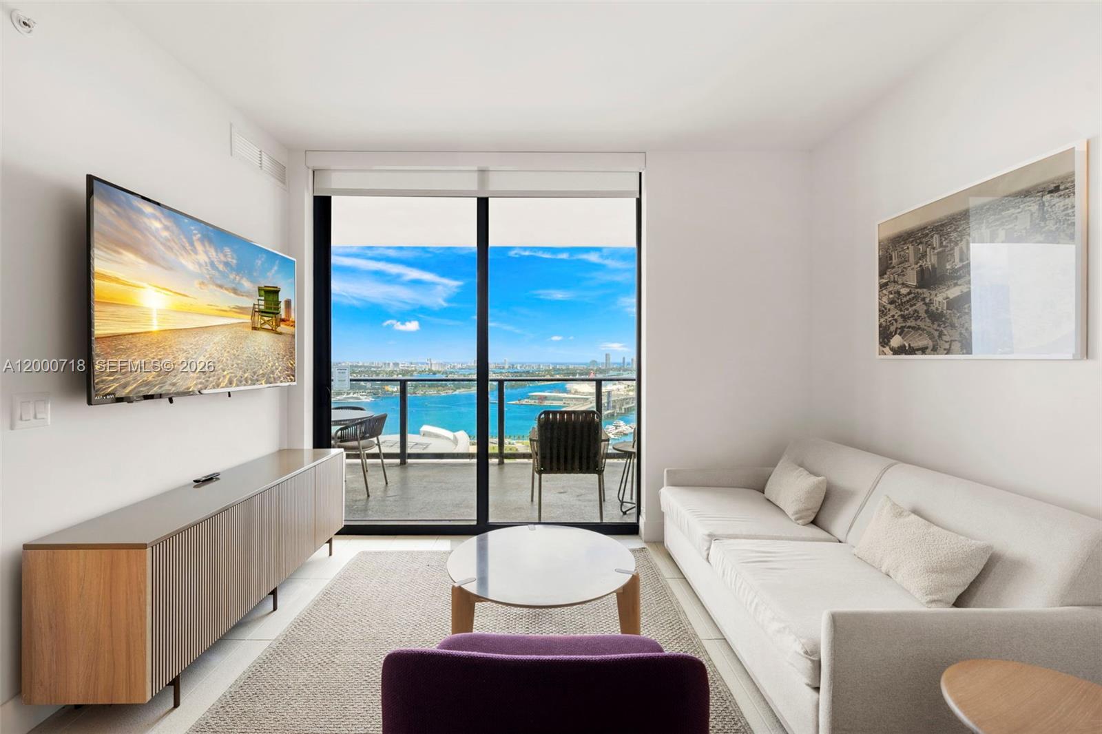 A living room features a white sofa, purple chair, television, and balcony with water views — 159 NE 6th St # 2915, Miami FL 33132, MIAMI, FL