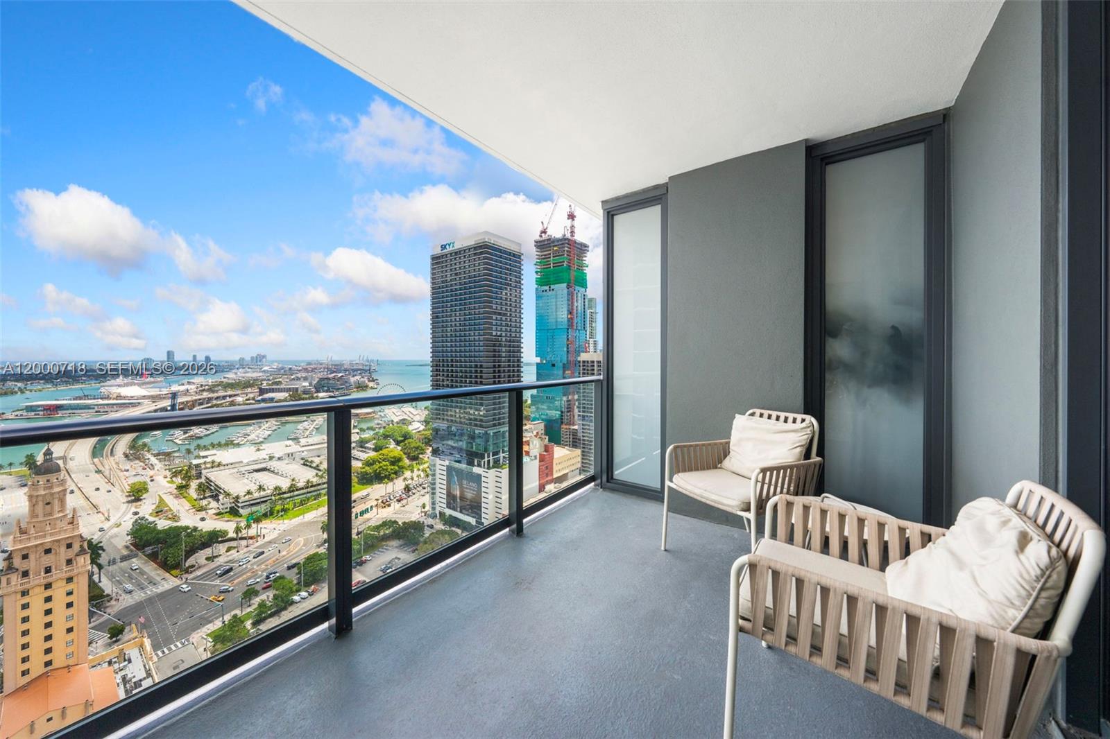 A high-rise balcony features two chairs and a panoramic view of a city skyline — 159 NE 6th St # 2915, Miami FL 33132, MIAMI, FL