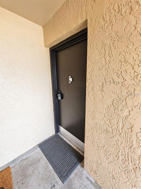 A dark-colored door with a lockbox and peephole is set in a textured beige wall — 5820 N CHURCH AVENUE UNIT 112, TAMPA, FL
