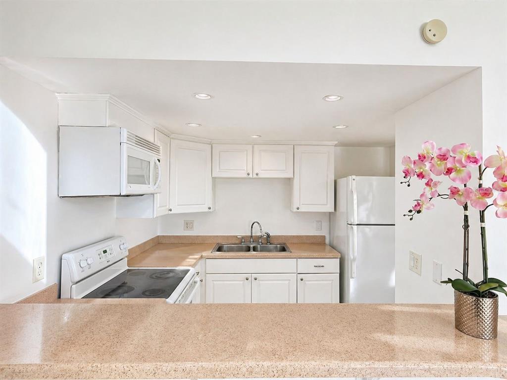 A kitchen features white cabinets, tan countertops, a white stove, and a white refrigerator — 5820 N CHURCH AVENUE UNIT 112, TAMPA, FL