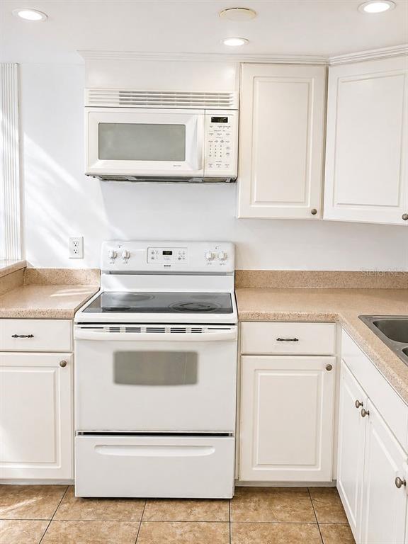 A kitchen features white cabinets, a white electric range, a microwave, and tan countertops — 5820 N CHURCH AVENUE UNIT 112, TAMPA, FL