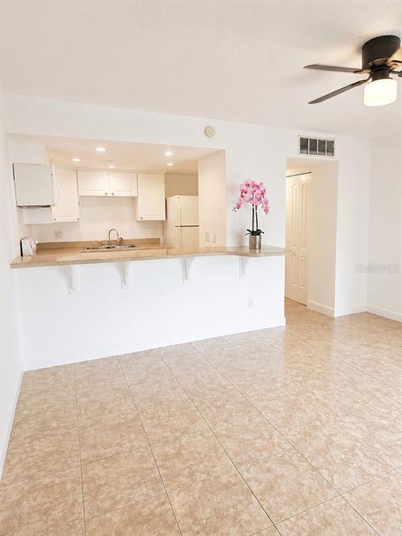 A kitchen with white cabinets and a breakfast bar overlooks a tiled living area — 5820 N CHURCH AVENUE UNIT 112, TAMPA, FL