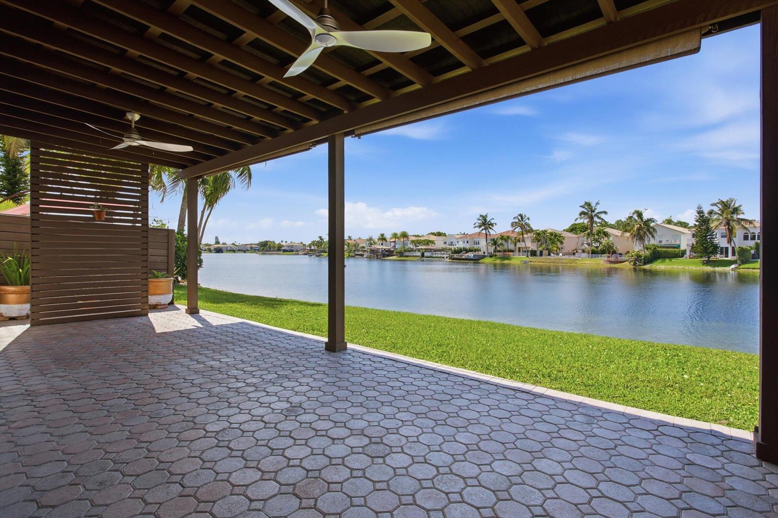 A covered patio with a paver floor overlooks a lake and residential houses — 11180 NW 73rd Street, Doral FL 33178, DORAL, FL