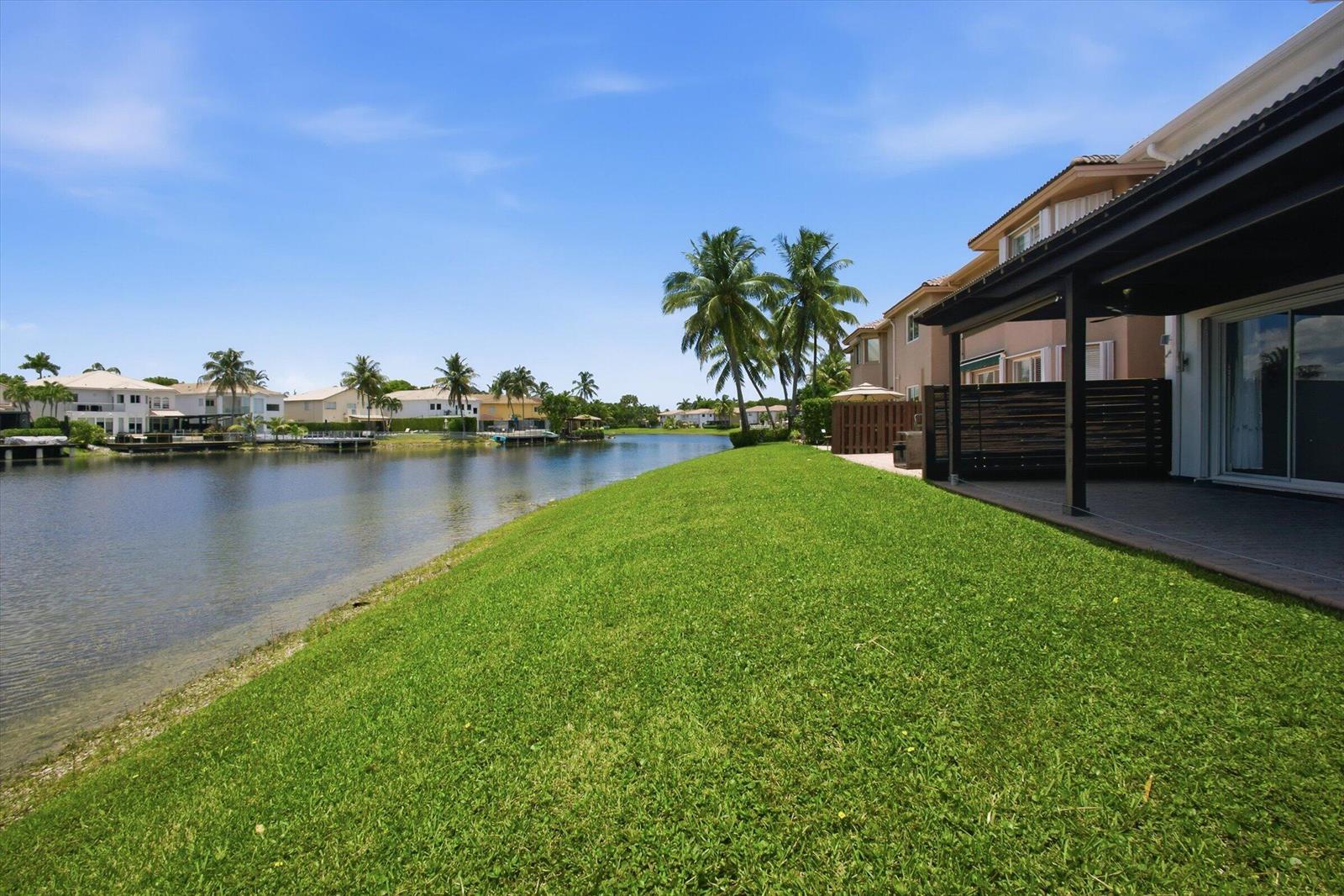 A grassy backyard slopes down to a canal behind a multi-story residential building — 11180 NW 73rd Street, Doral FL 33178, DORAL, FL