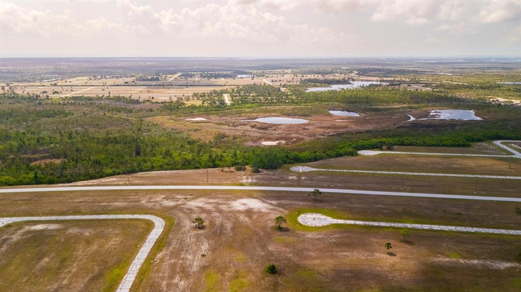 An aerial view shows a paved road network winding through undeveloped, grassy land with ponds — 12149 SALITPA COURT, PLACIDA, FL