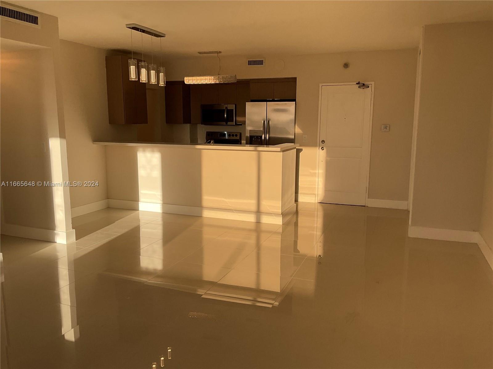 An open-concept kitchen features stainless steel appliances, dark cabinetry, and a breakfast bar — 10185 Collins Ave # 406, Bal Harbour FL 33154, BAL HARBOUR, FL