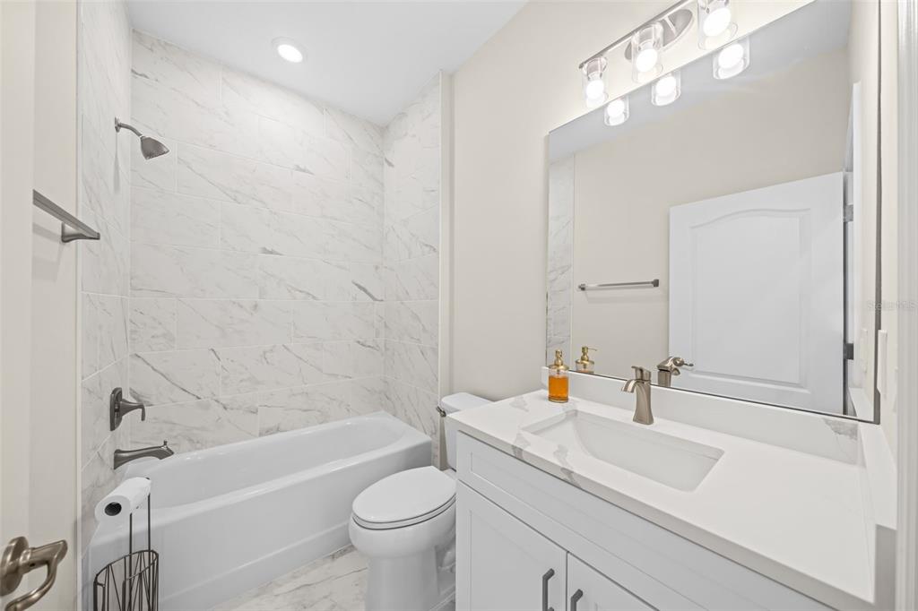 A bathroom features a white vanity, a toilet, and a bathtub with marble-look tile walls — 3121 LA FRANCE AVENUE SW, PALM BAY, FL