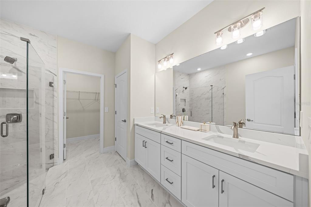 A modern bathroom features a double vanity with white cabinets, marble-look countertops, and a glass shower — 3121 LA FRANCE AVENUE SW, PALM BAY, FL