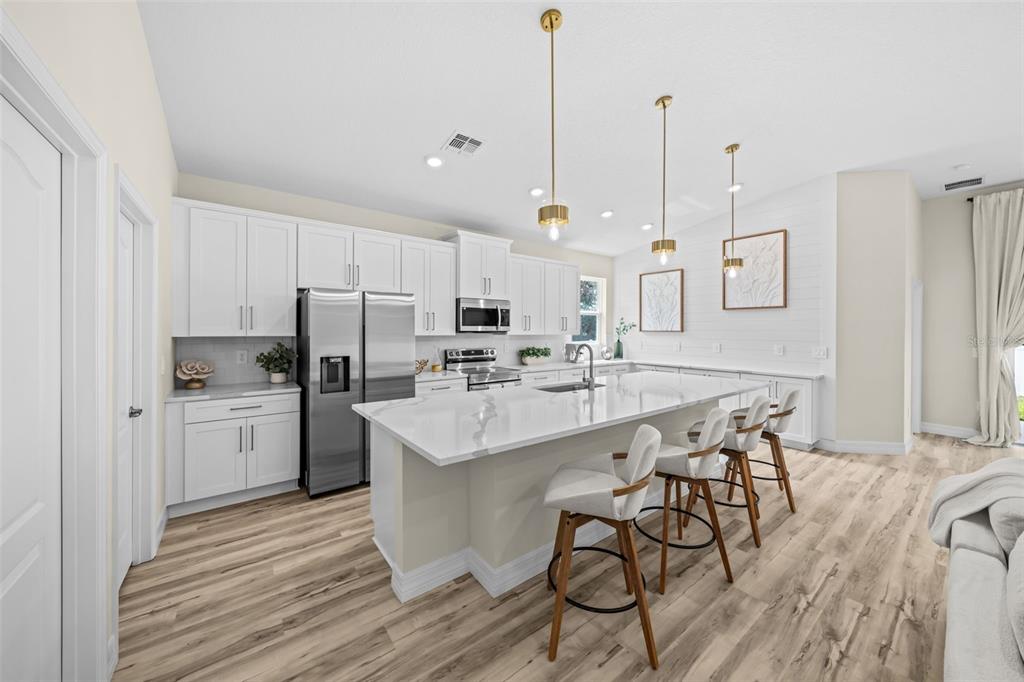 A modern kitchen features white cabinetry, a large marble-topped island with stools, and wood flooring — 3121 LA FRANCE AVENUE SW, PALM BAY, FL