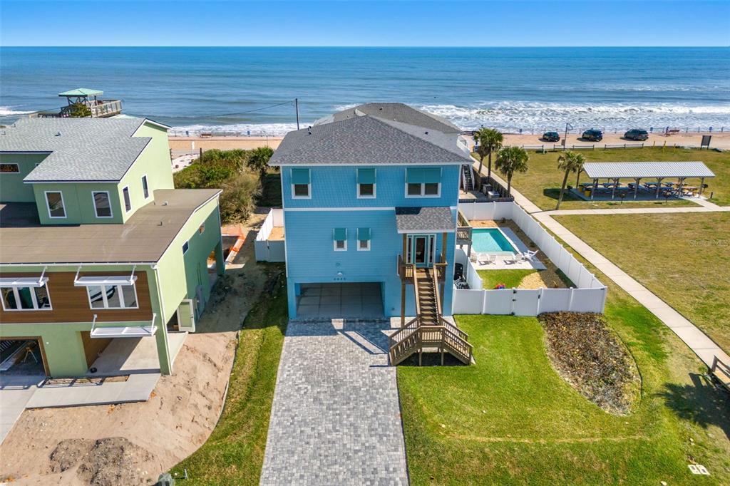 An aerial view shows a blue beach house with a pool, driveway, and oceanfront location — 6635 TURTLEMOUND ROAD, NEW SMYRNA BEACH, FL