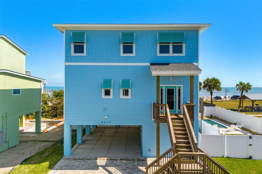 A blue, elevated stilt house features a front staircase, a ground-level carport, and a pool — 6635 TURTLEMOUND ROAD, NEW SMYRNA BEACH, FL