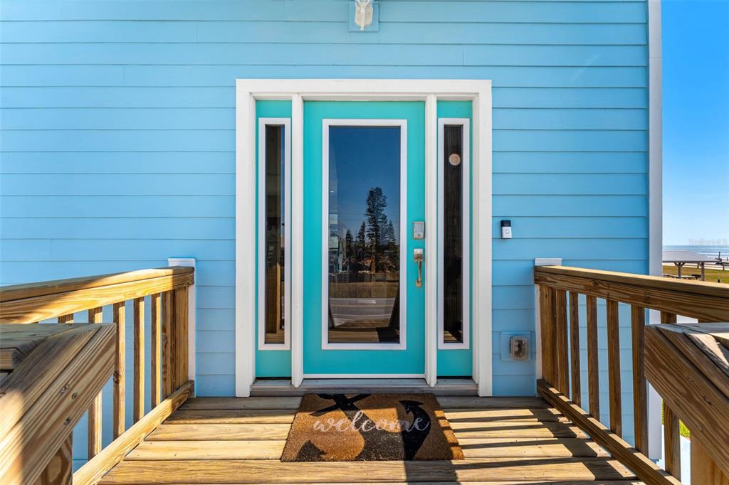 A turquoise front door with sidelights sits on a wooden deck of a blue house — 6635 TURTLEMOUND ROAD, NEW SMYRNA BEACH, FL